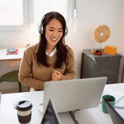 A woman happily video chatting on a laptop with headphones.