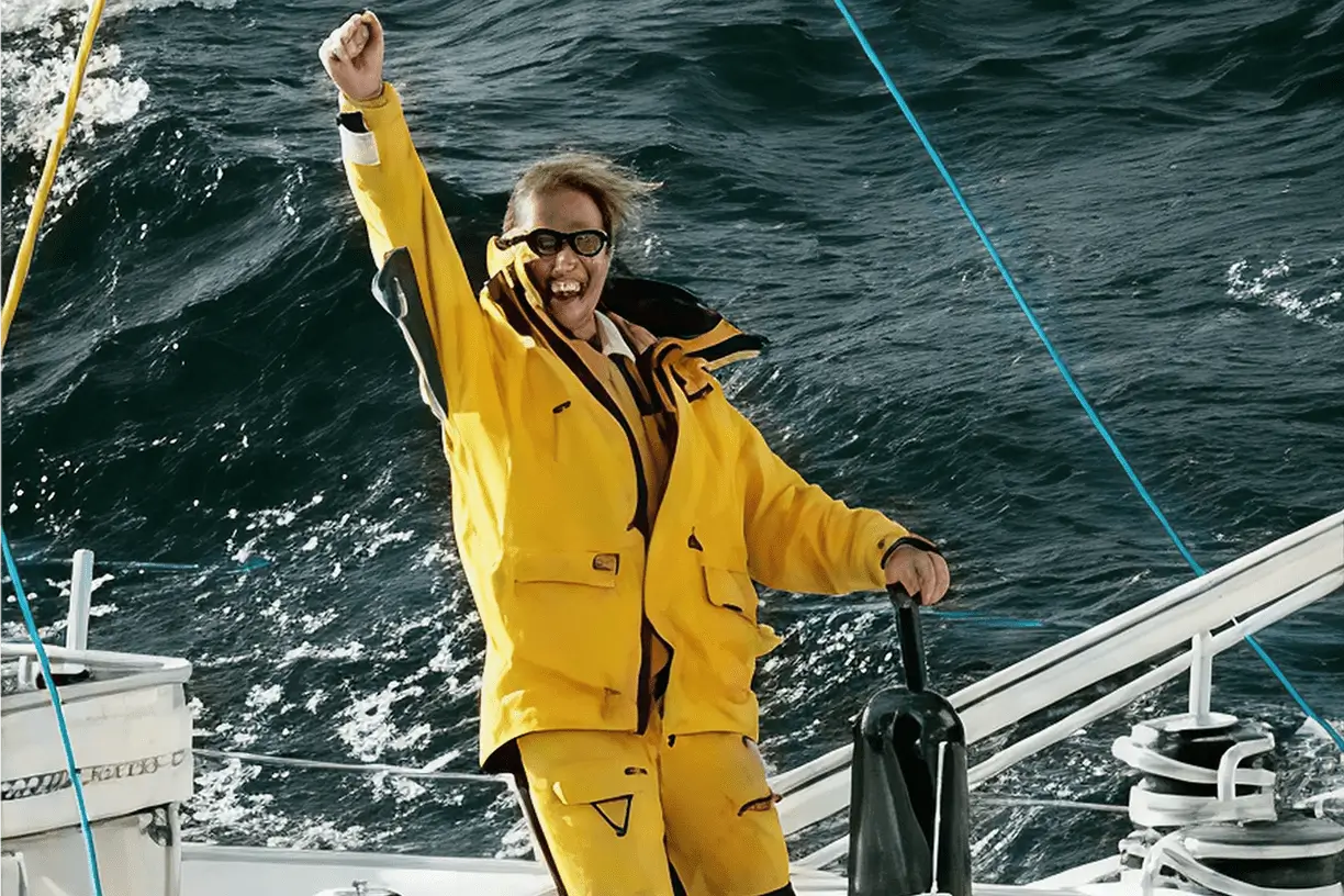 Person in yellow raincoat celebrating on boat.