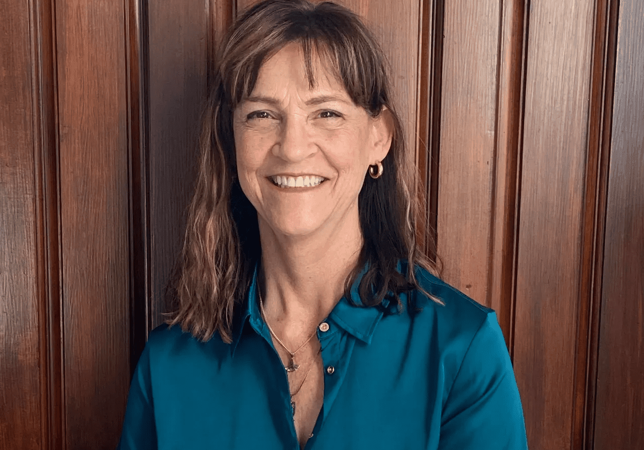 Smiling woman in teal blouse in front of wooden panel.